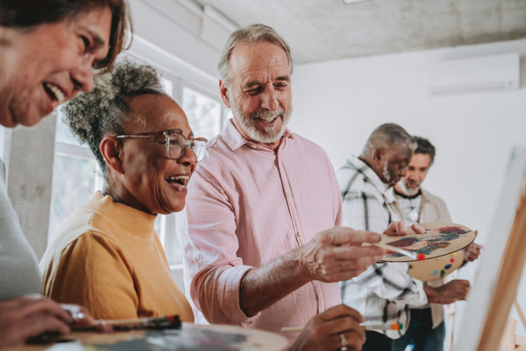 A group of seniors gathered around an easel, talking and painting