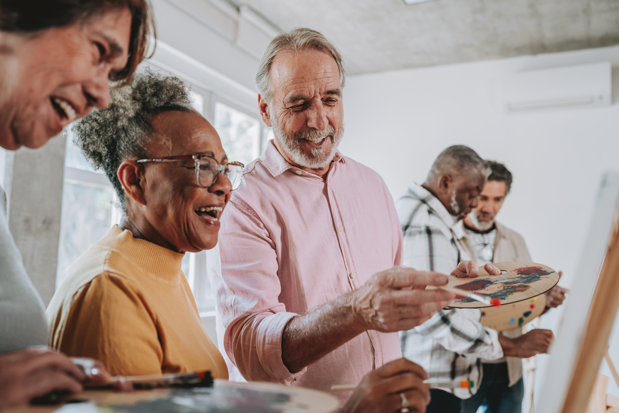 A group of seniors gathered around an easel, talking and painting